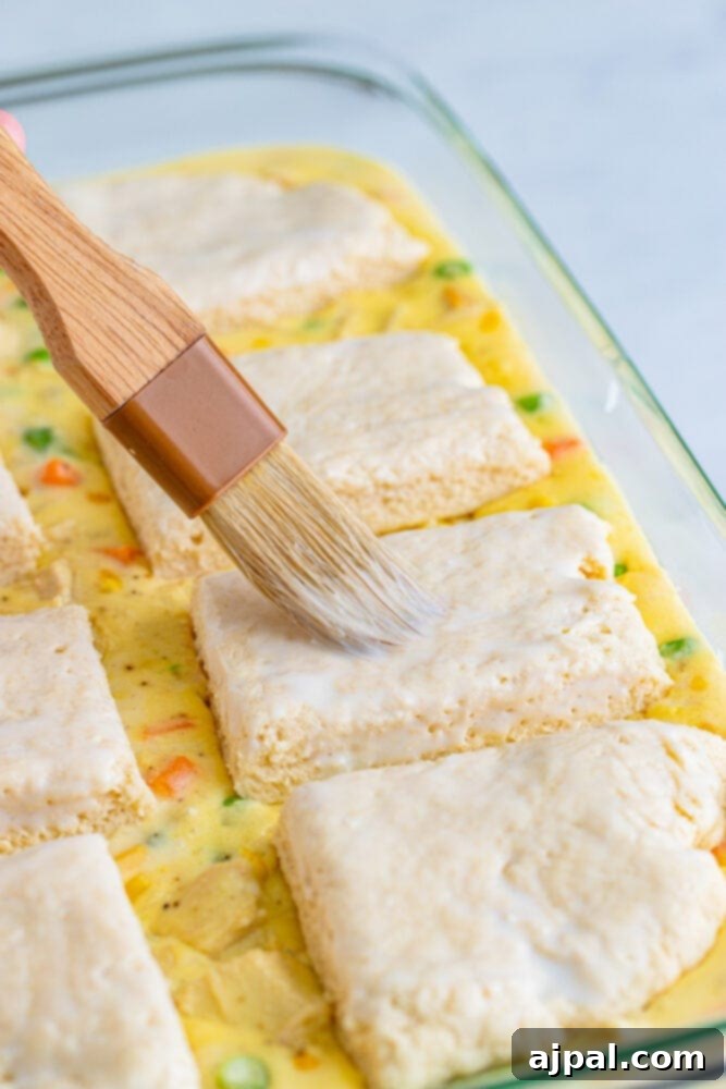 A pastry brush applying a light coat of buttermilk to the tops of the biscuit dough before baking, for a golden crust.