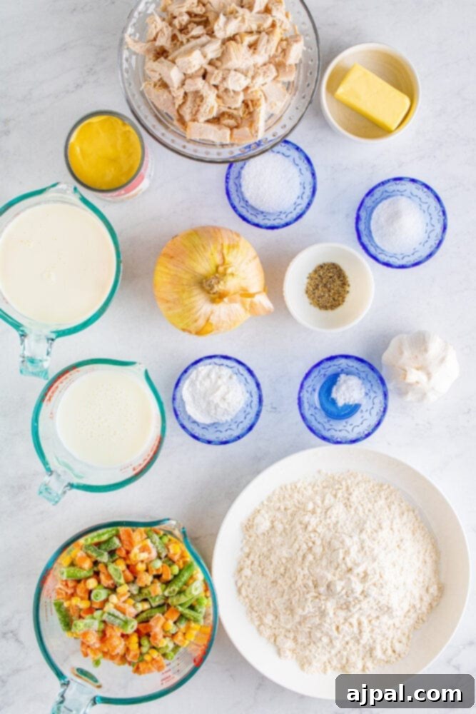 Assortment of turkey pot pie ingredients laid out on a table: butter, onions, garlic, frozen veggies, half and half, cream of chicken soup, cooked turkey, pepper, salt, flour, baking powder, sugar, baking soda, and buttermilk.