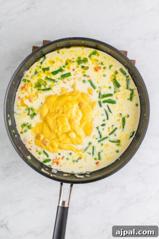 Cream of chicken soup being added to the pan with half and half and vegetables, being whisked to combine.