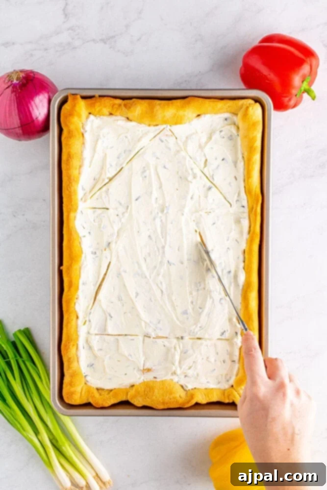 A butter knife delicately sketches the outline of a Christmas tree onto the cream cheese layer, preparing for vegetable decoration.