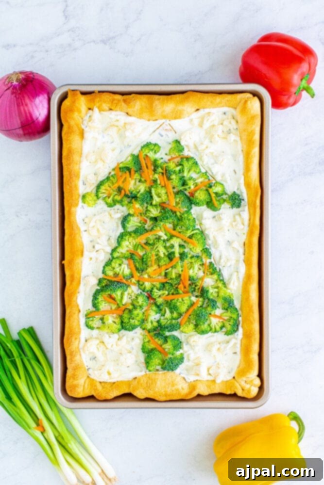 The Christmas tree pizza takes shape with broccoli, red onions, and grated carrots adding layers of color and texture.