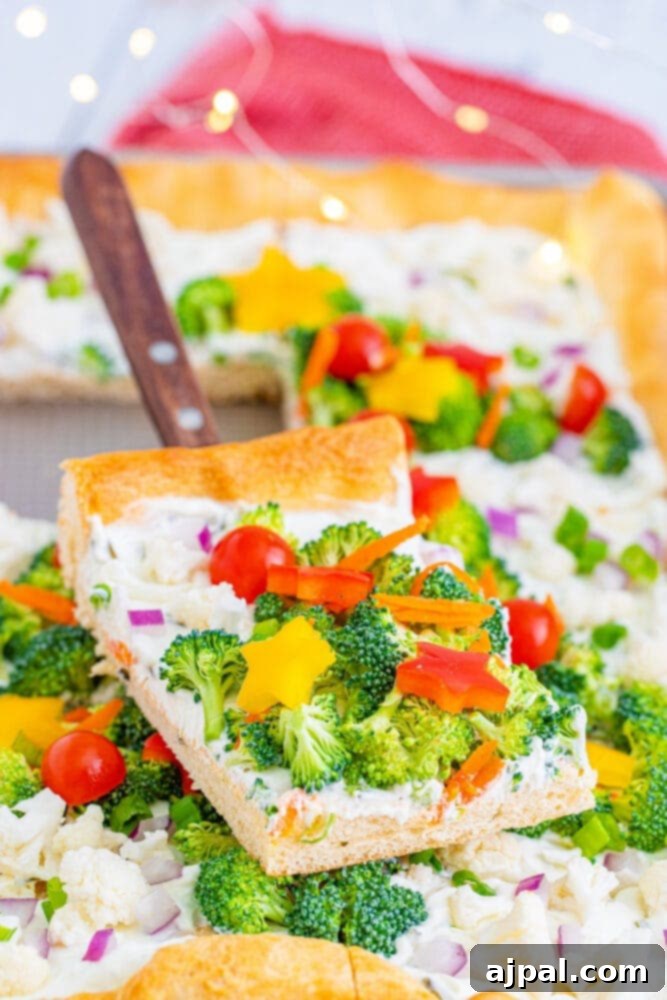 A slice of Christmas tree vegetable pizza with bright, fresh toppings sits on a white plate, ready to be enjoyed.