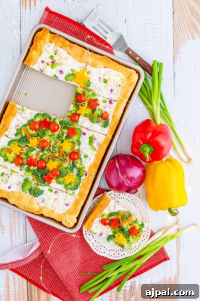 A close-up of a single slice of Christmas tree vegetable pizza on a white plate, showcasing the colorful vegetable toppings and fluffy crust.