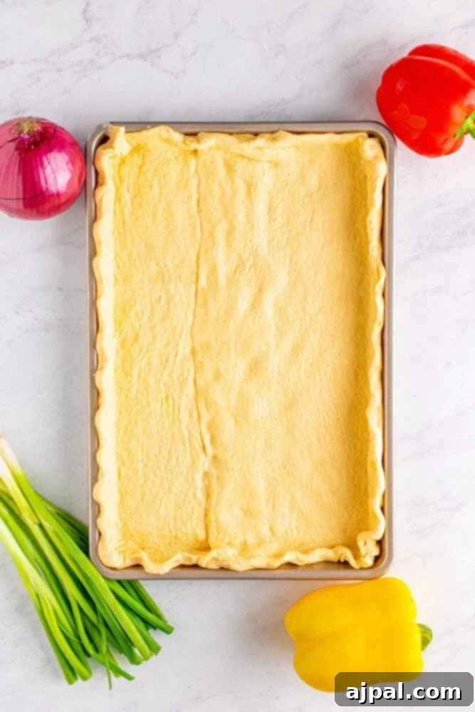 Raw crescent dough sheets are carefully overlapped on a baking sheet, with seams pinched together, preparing for baking.