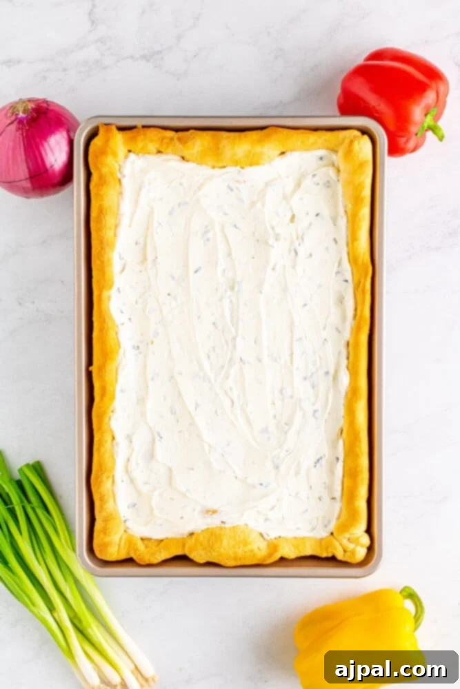 A creamy chive and sour cream spread is expertly applied to the cooled, baked crescent dough crust, leaving a neat border.