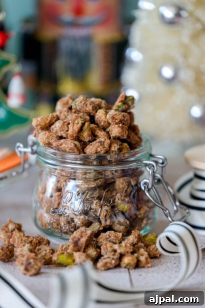 A glass jar filled with perfectly candied pistachios, featuring a sweet and salty glaze with visible cinnamon. Ideal for holiday treats or gifting.