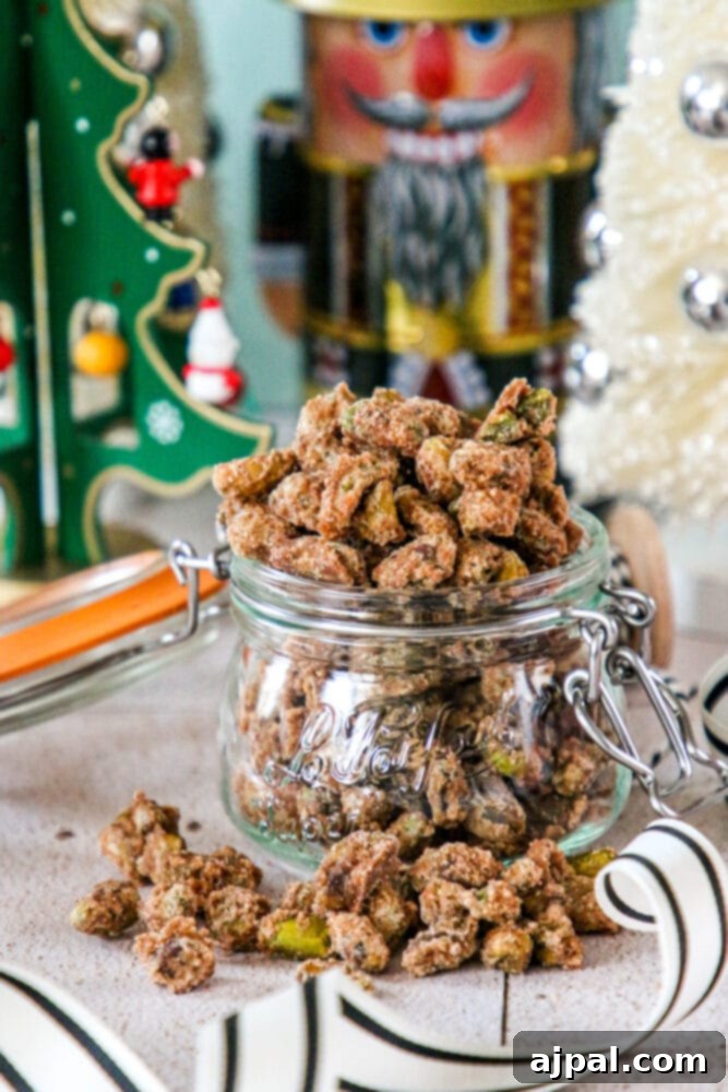 A festive glass jar overflowing with candied pistachios and decorated with a cinnamon stick, perfect for holiday gifting or entertaining.