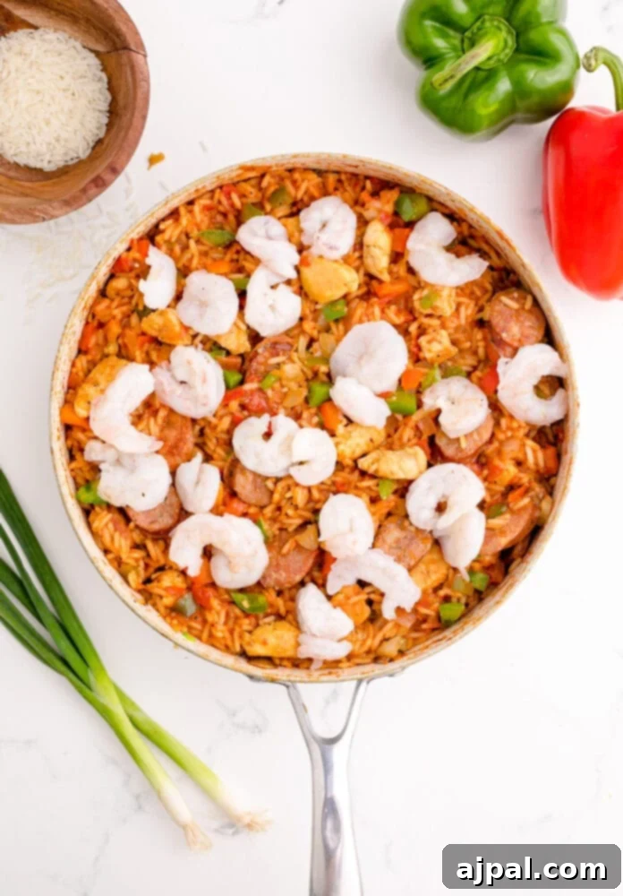 picture of jambalaya with cooked rice in a pan with raw shrimp on top