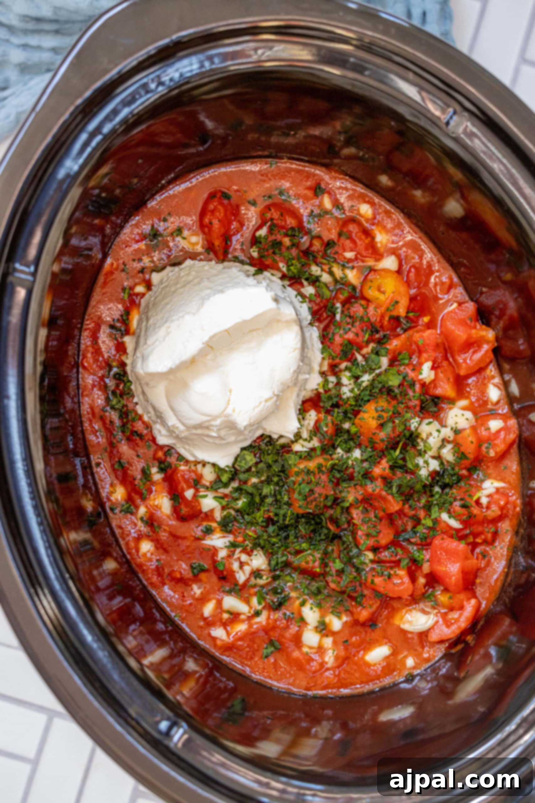 picture of diced tomatoes, pasta sauce, basil, cream cheese, and garlic in a slow cooker