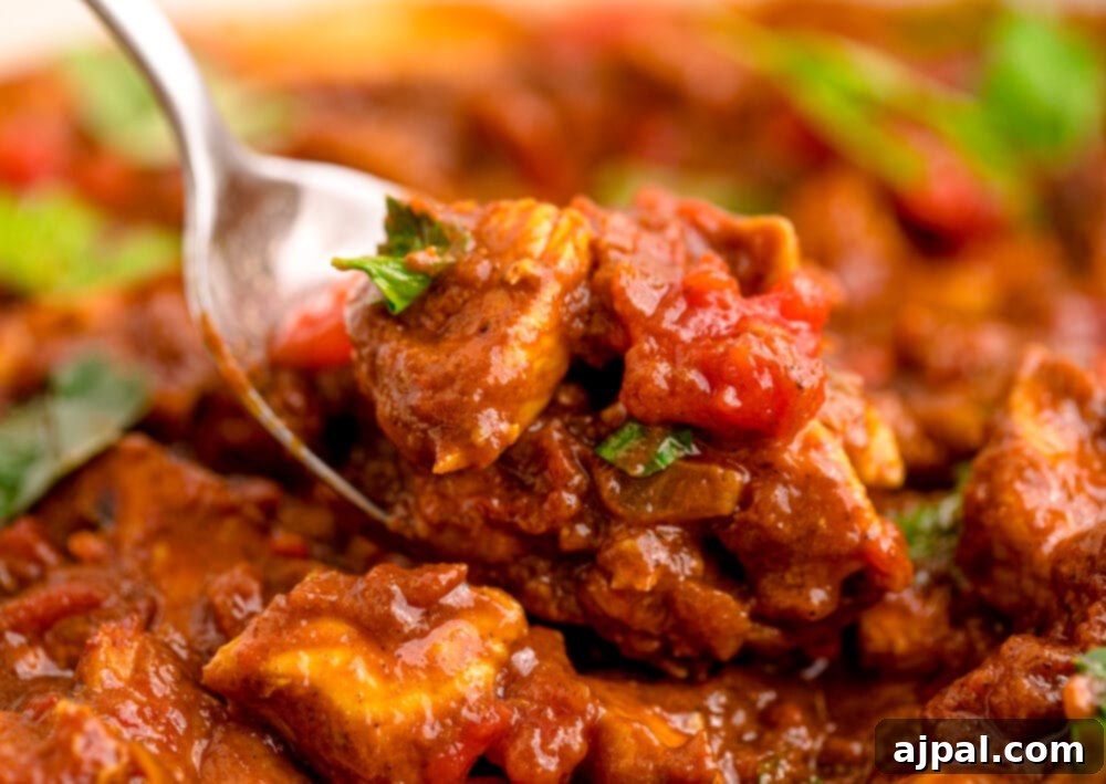 A close-up of a spoon scooping a generous portion of creamy Chicken Madras Curry from a pan, highlighting its vibrant color and tender chicken pieces.