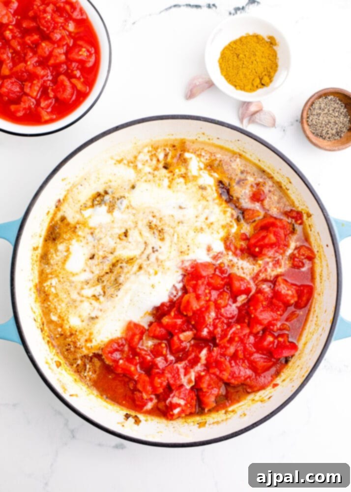 A pan with sautéed vegetables and spices, including diced tomatoes and onions, infused with rich curry aromas.