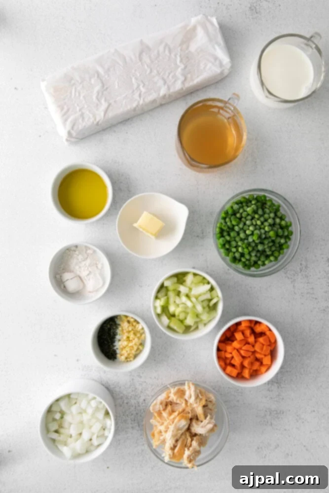 A vibrant assortment of fresh vegetables, shredded chicken, and flaky puff pastry are neatly arranged on a table, showcasing the key ingredients for delicious individual chicken pot pies.