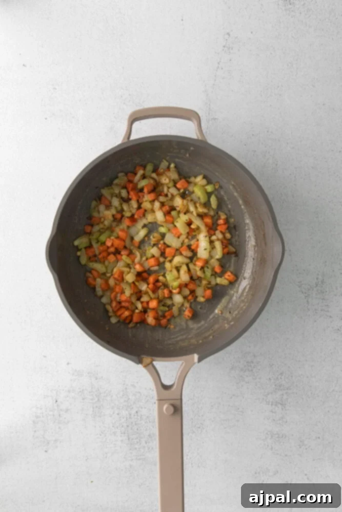 Fresh vegetables, including chopped onions, carrots, and celery, are shown browning in a pan, releasing their aromatic flavors.