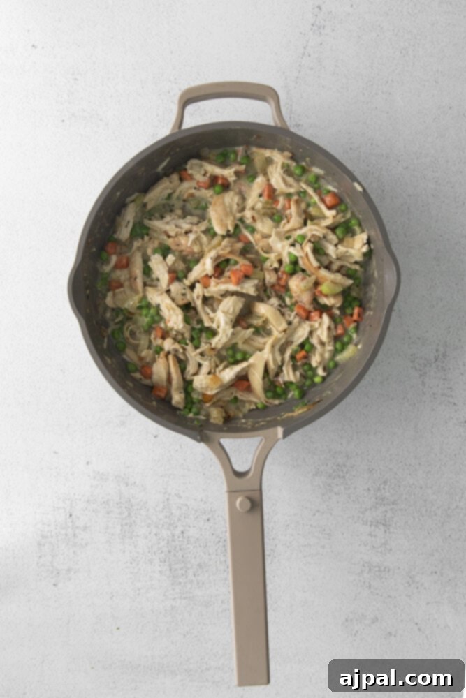 Shredded chicken and sautéed vegetables are mixed together in a pan, forming the flavorful base of the pot pie filling.