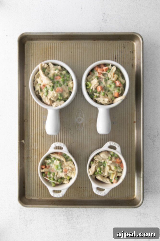 A creamy, rich chicken pot pie filling, generously portioned into a white ramekin, awaits its puff pastry topping.