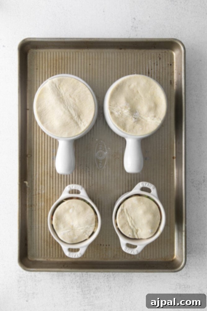 A perfectly cut puff pastry circle is placed over a ramekin filled with chicken pot pie mixture, ready for the oven.