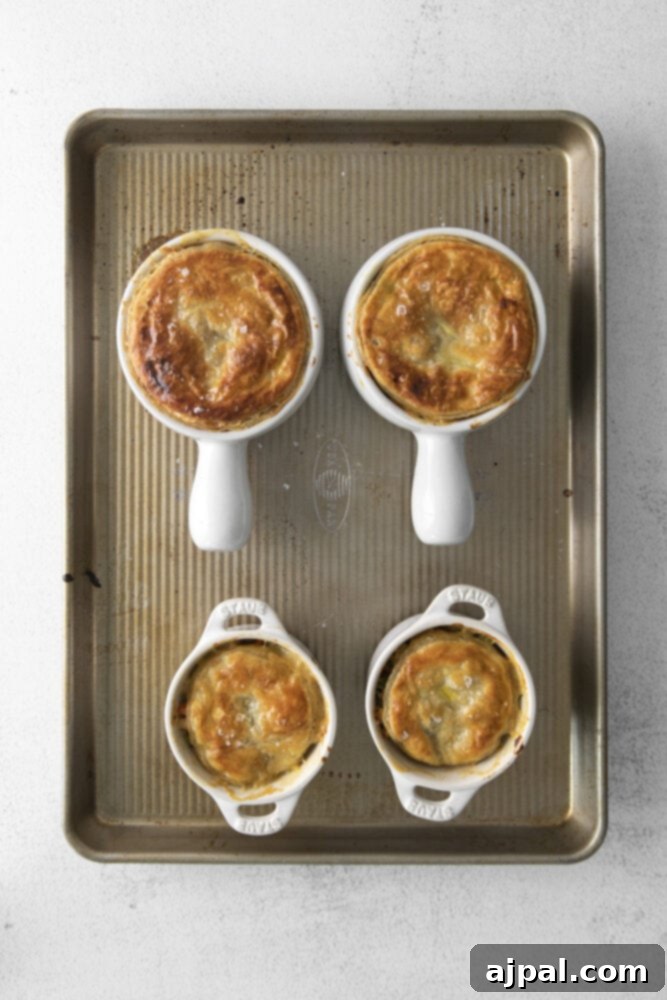 A baking sheet holds several individual chicken pot pies, with their puff pastry tops golden and puffed, freshly baked from the oven.