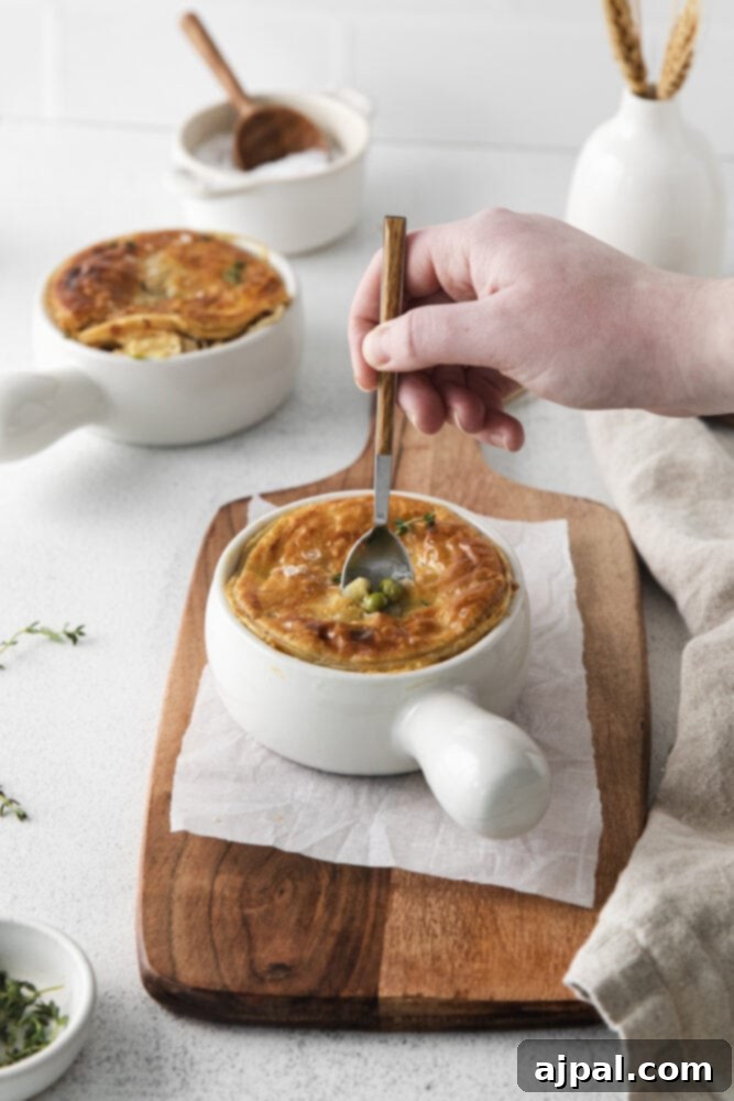A spoon dips into a hot, individual chicken pot pie in a white ramekin, revealing the creamy filling and flaky crust.