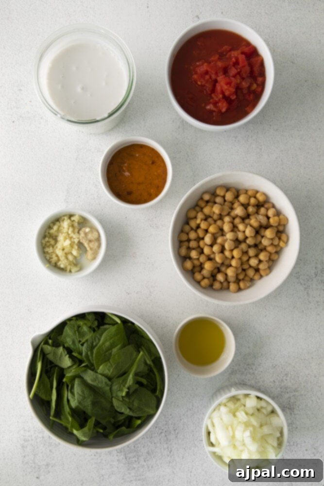 A collection of fresh ingredients for vegan chickpea curry laid out on a table, including chickpeas, spinach, ginger, garlic, and red curry paste, ready for preparation.