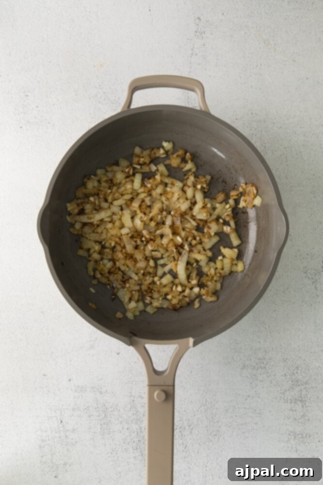 Finely diced onions, garlic, and ginger sautéing in a pan, releasing their aromatic fragrances as they cook down to a translucent base for the curry.