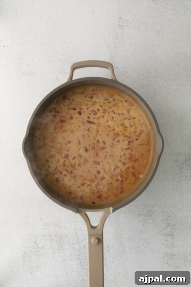 The rich red curry paste, diced tomatoes, and creamy coconut milk simmering together in a saucepan, forming the vibrant and fragrant sauce for the chickpea curry.