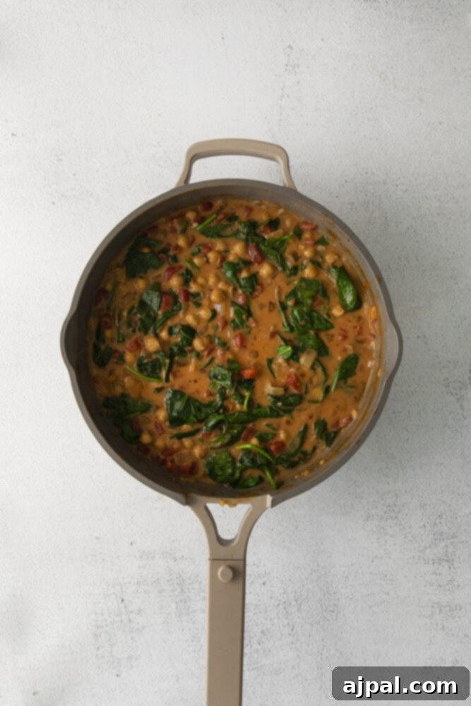 Fresh baby spinach leaves wilting into the simmering chickpea curry, adding a touch of vibrant green and healthy goodness to the dish.