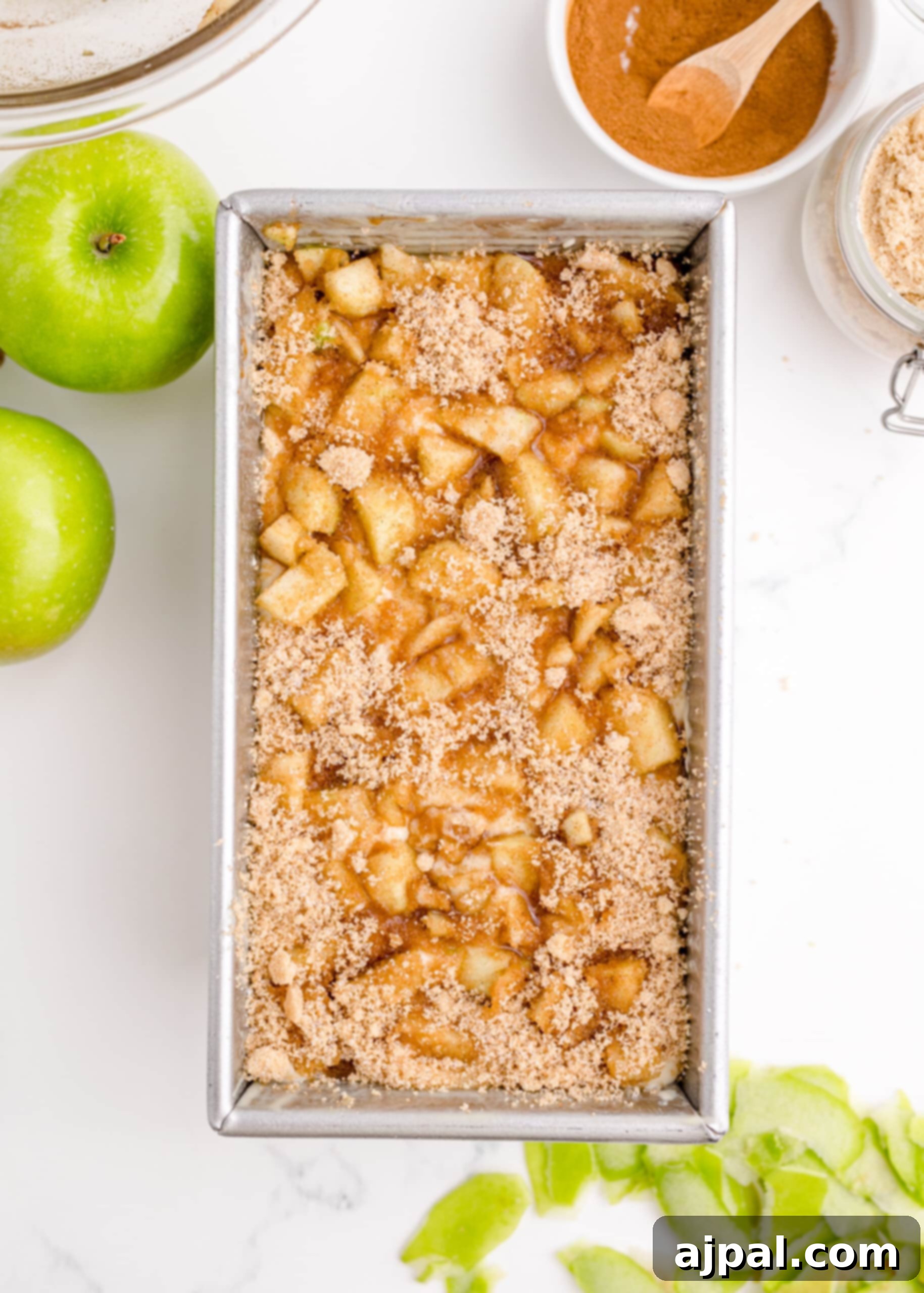 Picture of apples and brown sugar topping generously layered over the batter in a loaf pan before baking.