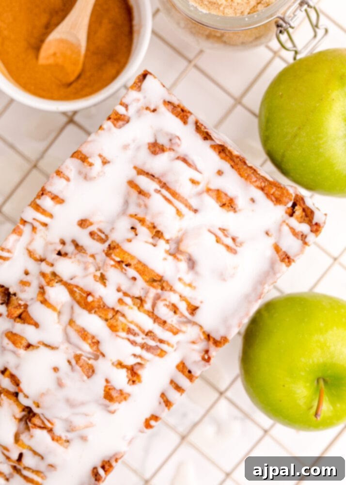 Close-up of a warm apple fritter sweet bread loaf drizzled with white icing and garnished with apple slices.