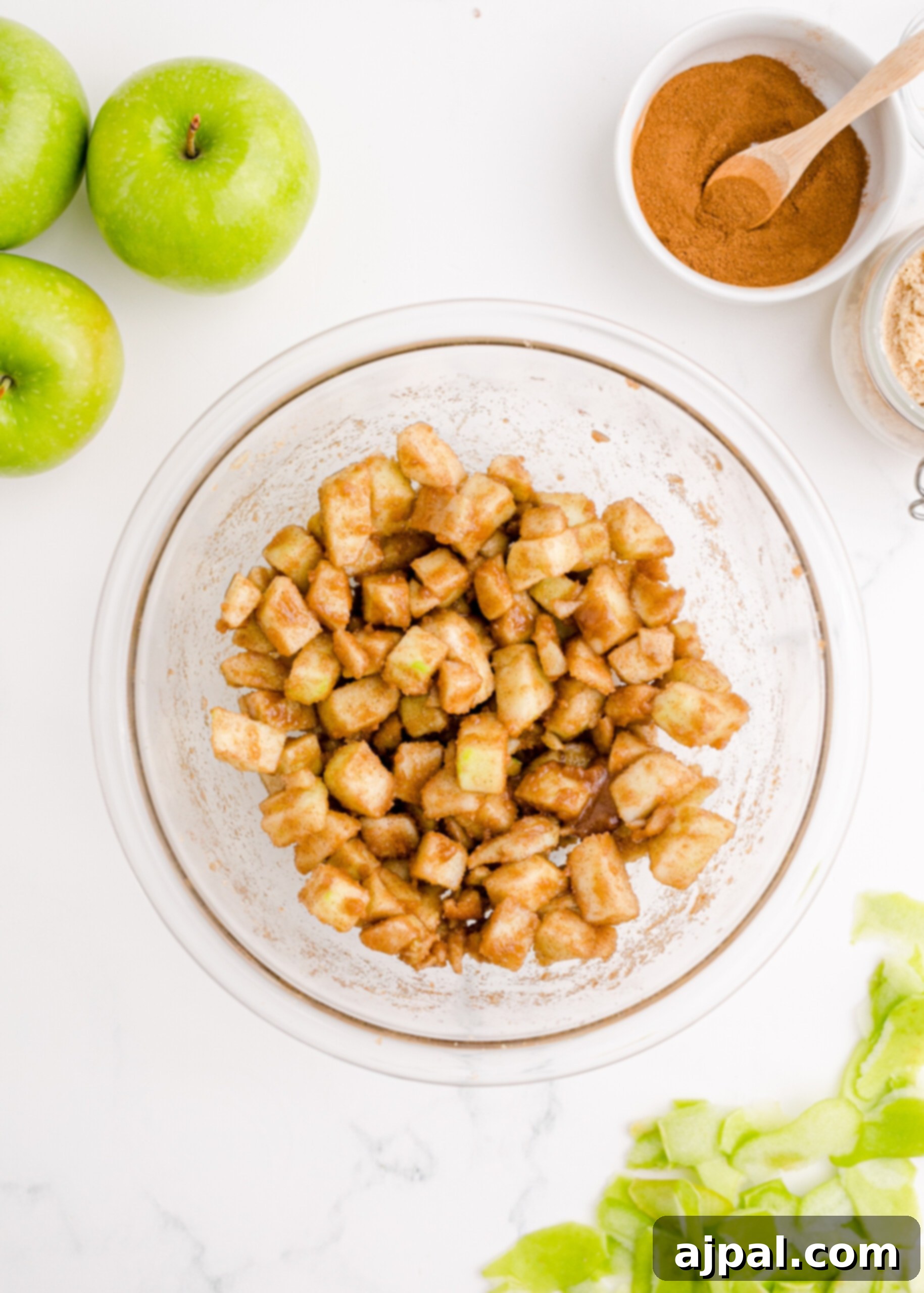 Diced apples being mixed with a rich cinnamon sugar coating in a bowl.