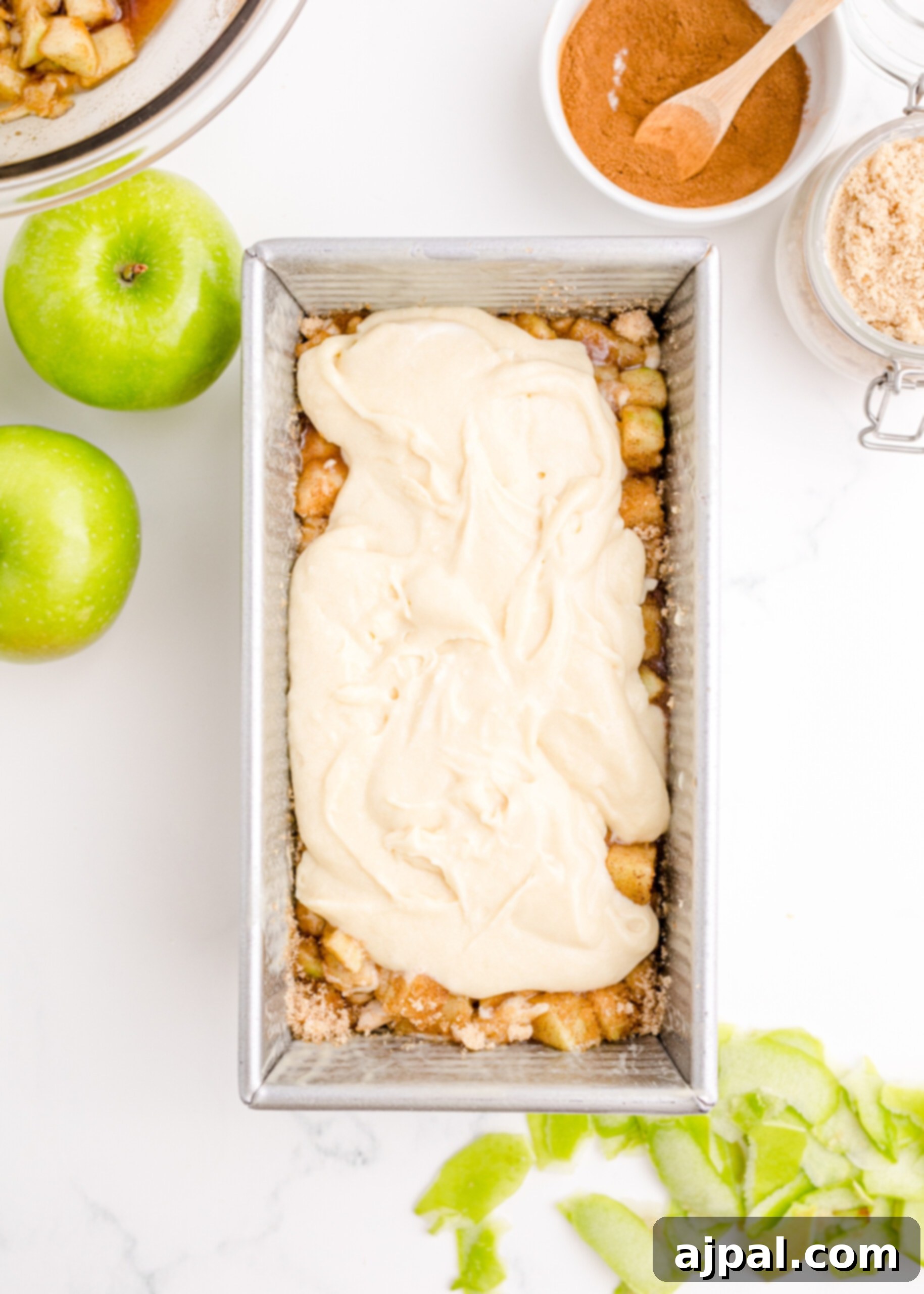 Picture of golden batter poured over a layer of spiced apples in a loaf pan, ready for more layers.