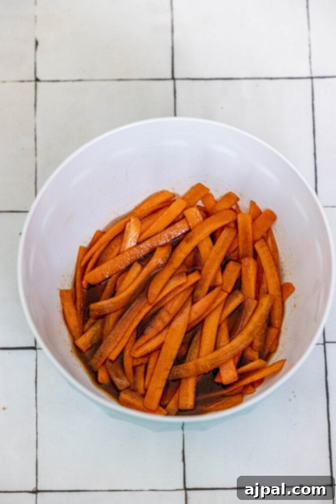 Thinly sliced carrots marinating in a savory, smoky sauce in a glass bowl, absorbing the rich flavors for the vegan bacon.