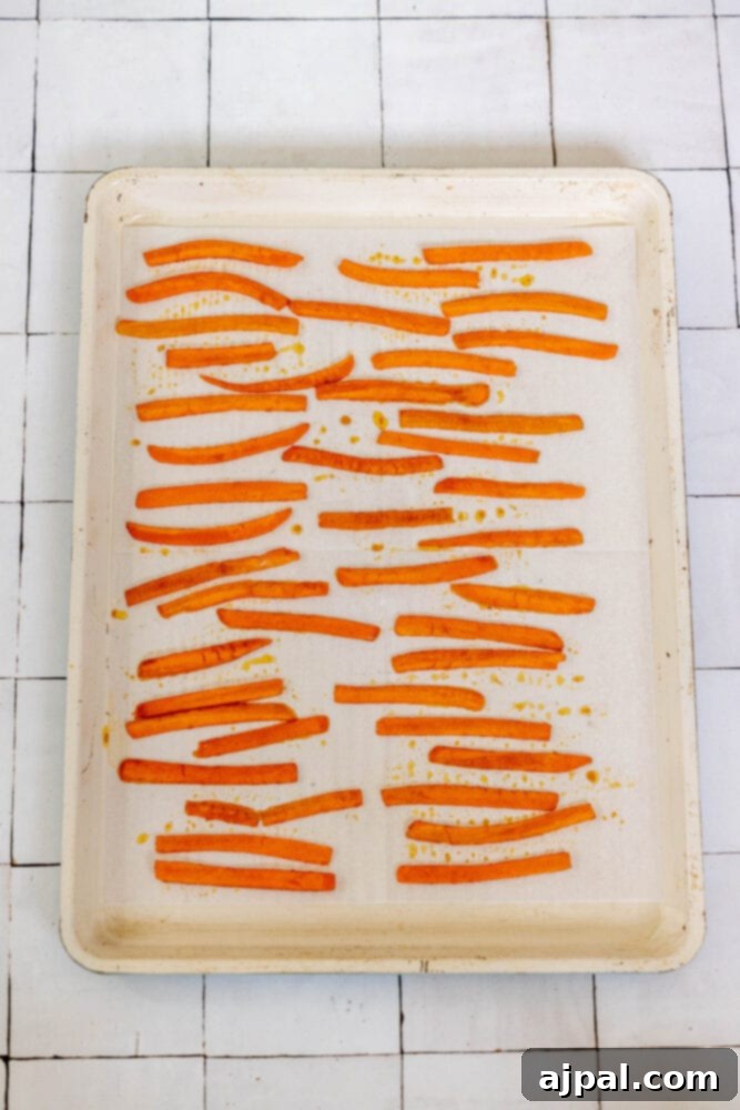 Marinated carrot strips meticulously arranged on a parchment-lined baking sheet, ready for the oven to transform into crispy vegan bacon.