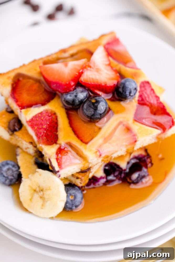 A plate featuring a stack of golden sheet pan pancakes generously drizzled with syrup and topped with a colorful medley of fresh berries and sliced bananas, inviting a delightful breakfast.