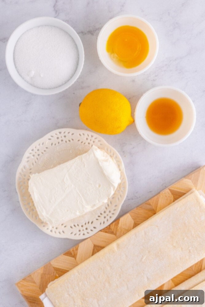 Various ingredients for the cheese danish recipe laid out on a table, including cream cheese, sugar, eggs, and a lemon.