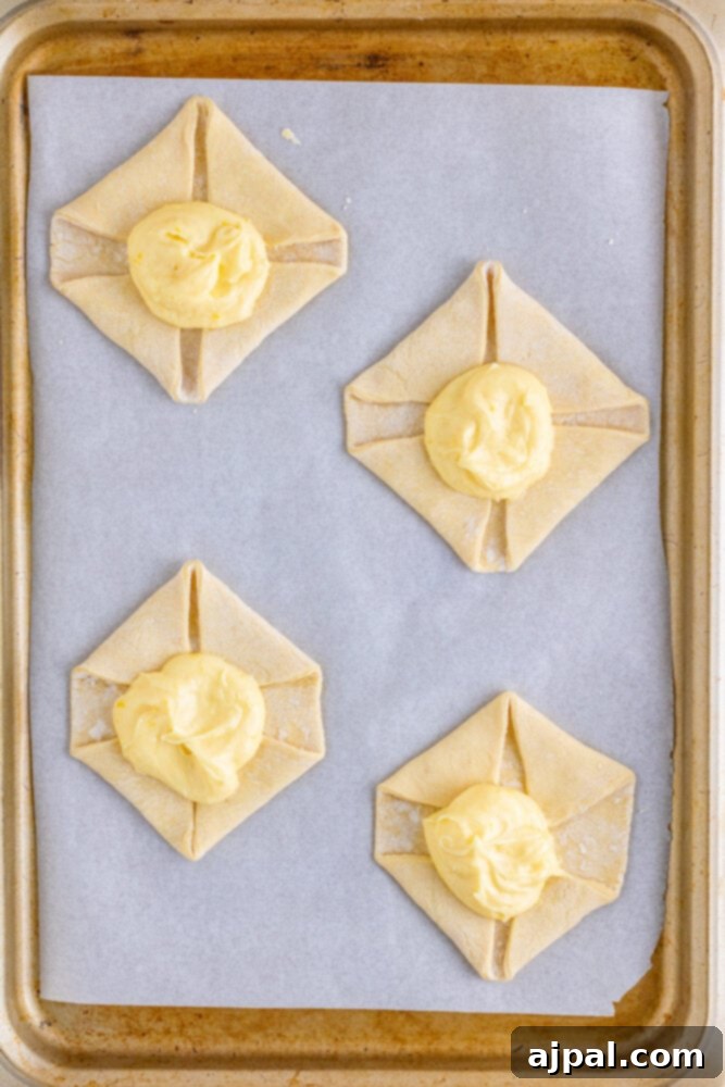 Puff pastry squares with a generous dollop of cheese filling in the center, ready for the oven.