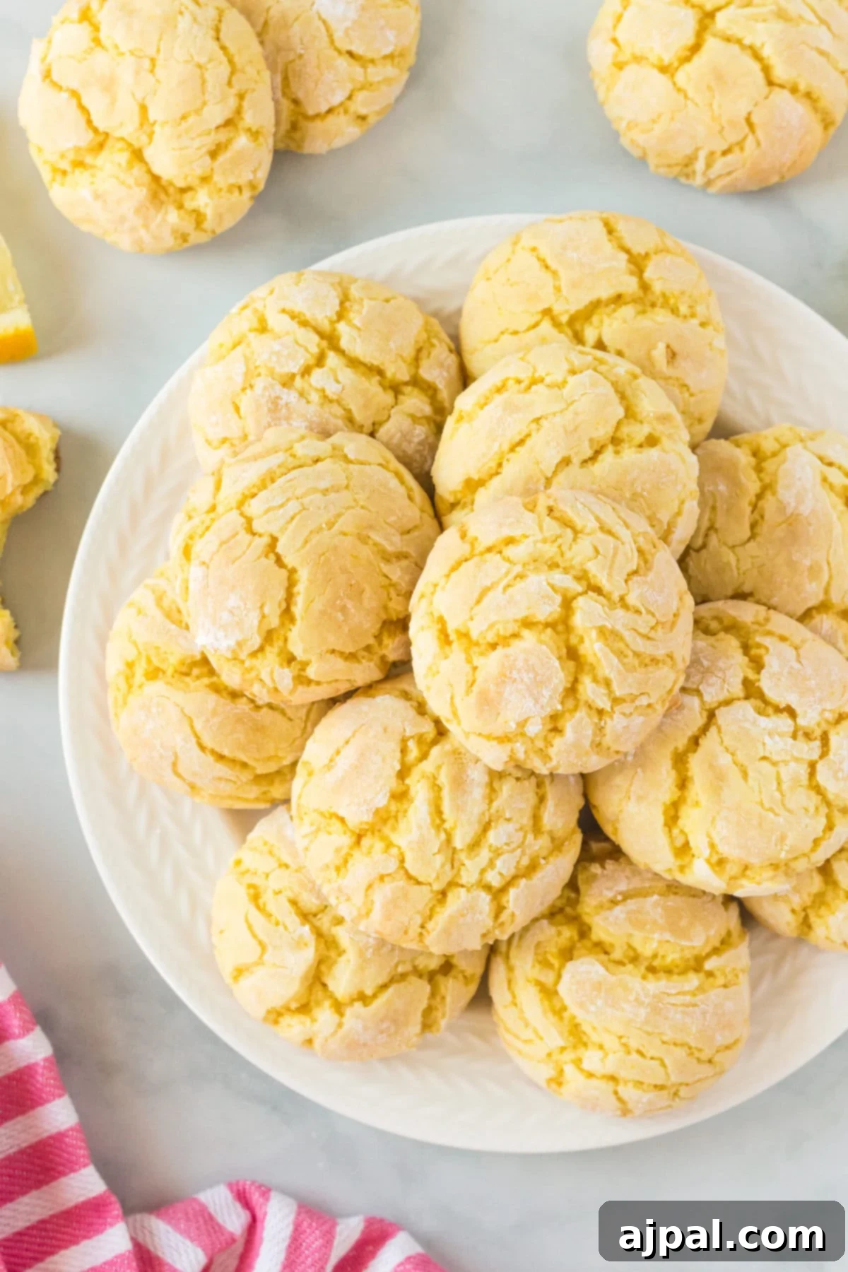 A generous pile of yellow lemon crinkle cookies, made with lemon cake mix, displayed on a pristine white plate.