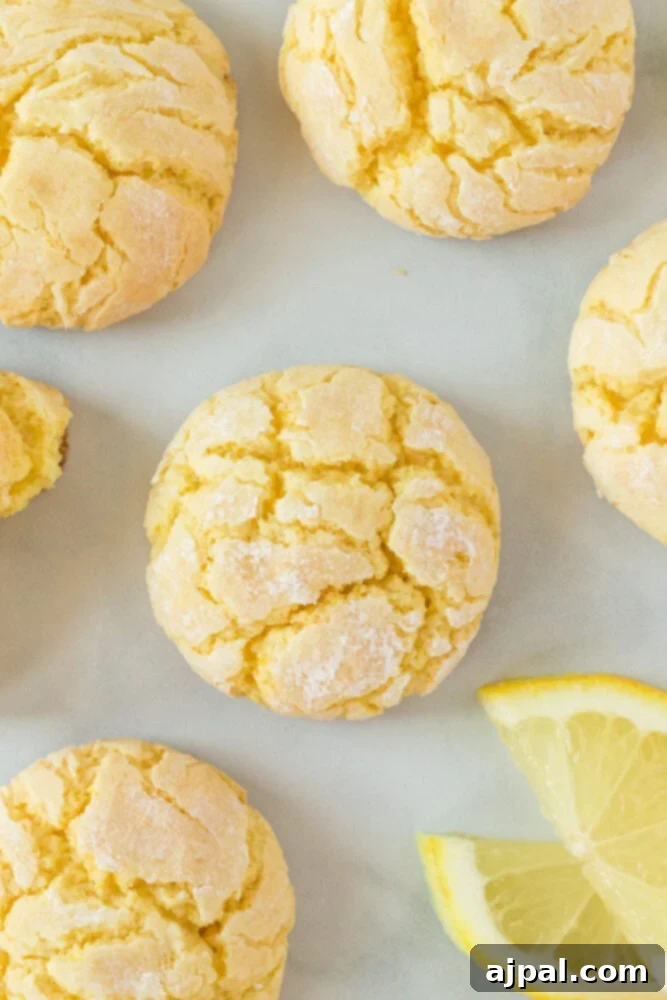 Close-up of fluffy, lemon crinkle cookies on a white surface, garnished with a fresh lemon slice, highlighting their vibrant citrus appeal.