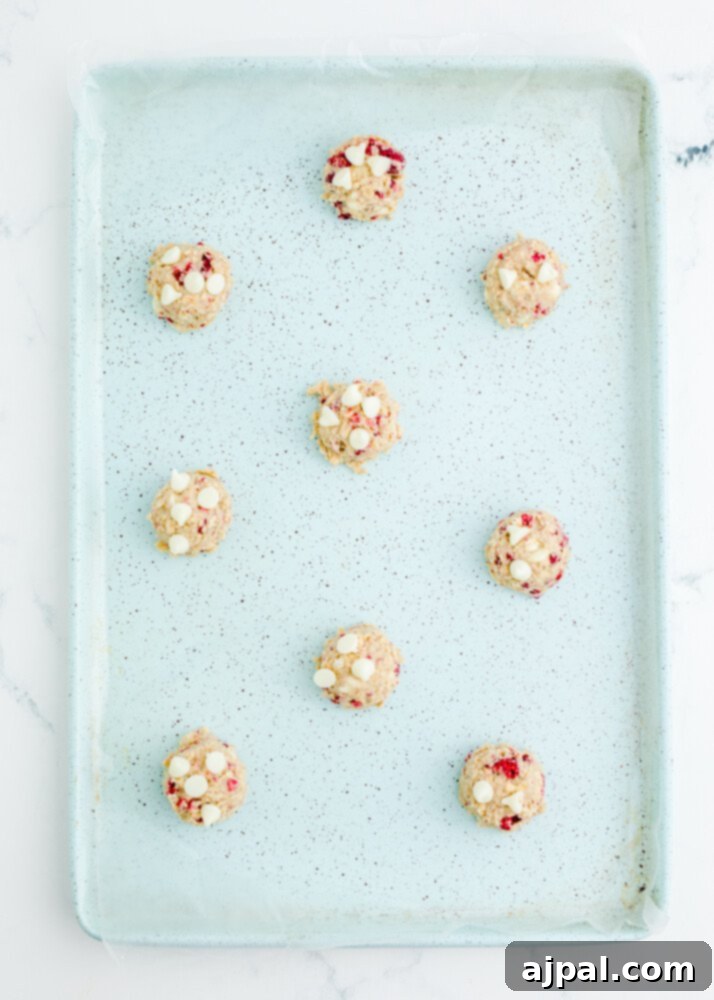 Another view of cookie dough in a scooper, showcasing the textures of oats, white chocolate chips, and flecks of raspberry.