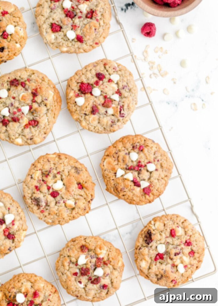 A close-up of several white chocolate raspberry oatmeal cookies cooling on a wire rack, showcasing their golden edges and plump texture.