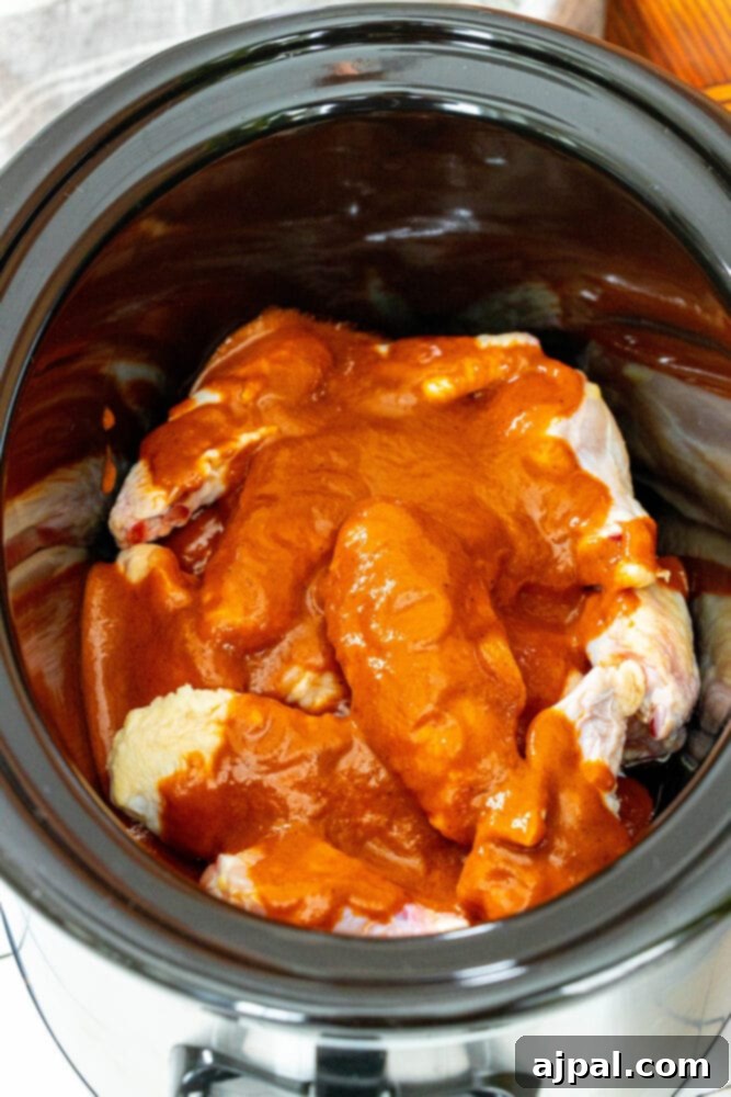 Smoky Tinga Slow Cooker Wings 6 Chicken wings coated in rich Tinga sauce, simmering in a slow cooker.