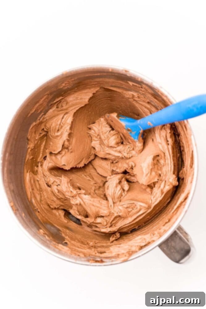 Ultimate Peanut Butter Cake 6 A bowl of creamy peanut butter frosting being mixed with a paddle attachment, achieving a smooth texture.