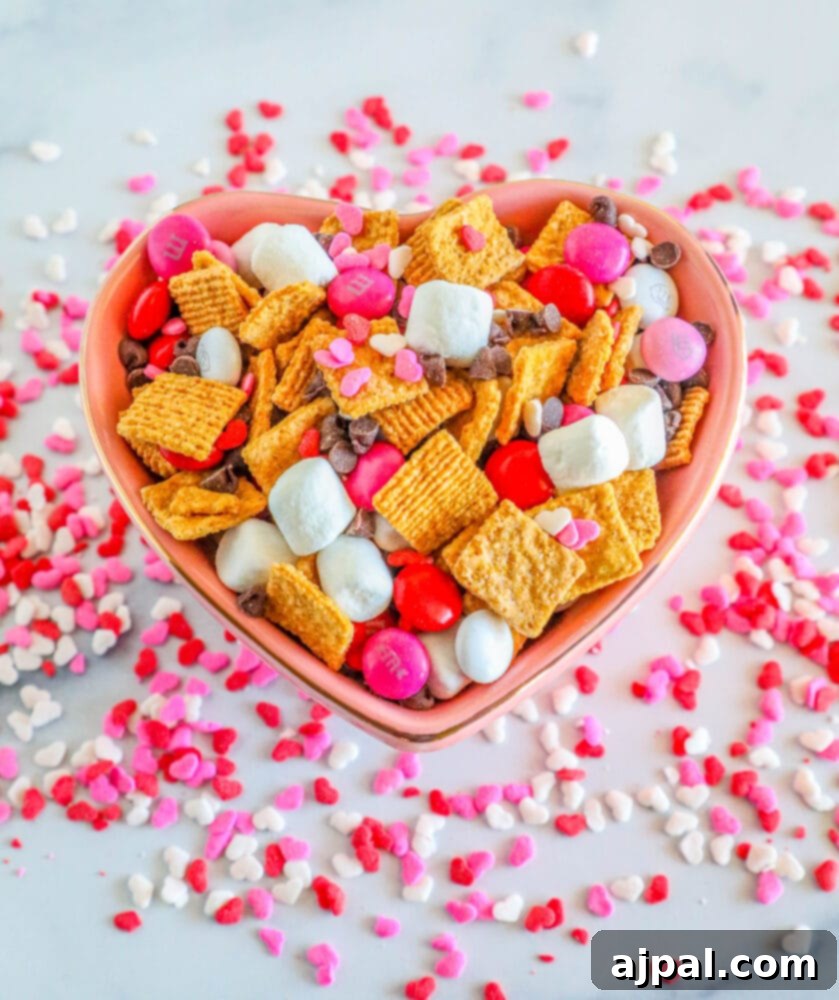 Valentine Smores Snack Mix 2 Heart-shaped bowl overflowing with a vibrant Valentine's S'mores Snack Mix, featuring marshmallows, pink M&M's, festive sprinkles, and mini chocolate chips.