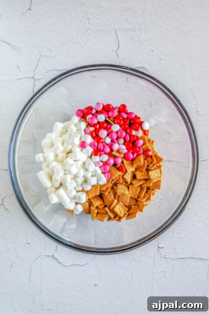 Valentine Smores Snack Mix 5 Golden Grahams cereal, mini marshmallows, and pink M&M's combined in a bowl, showcasing the first steps of the snack mix creation.