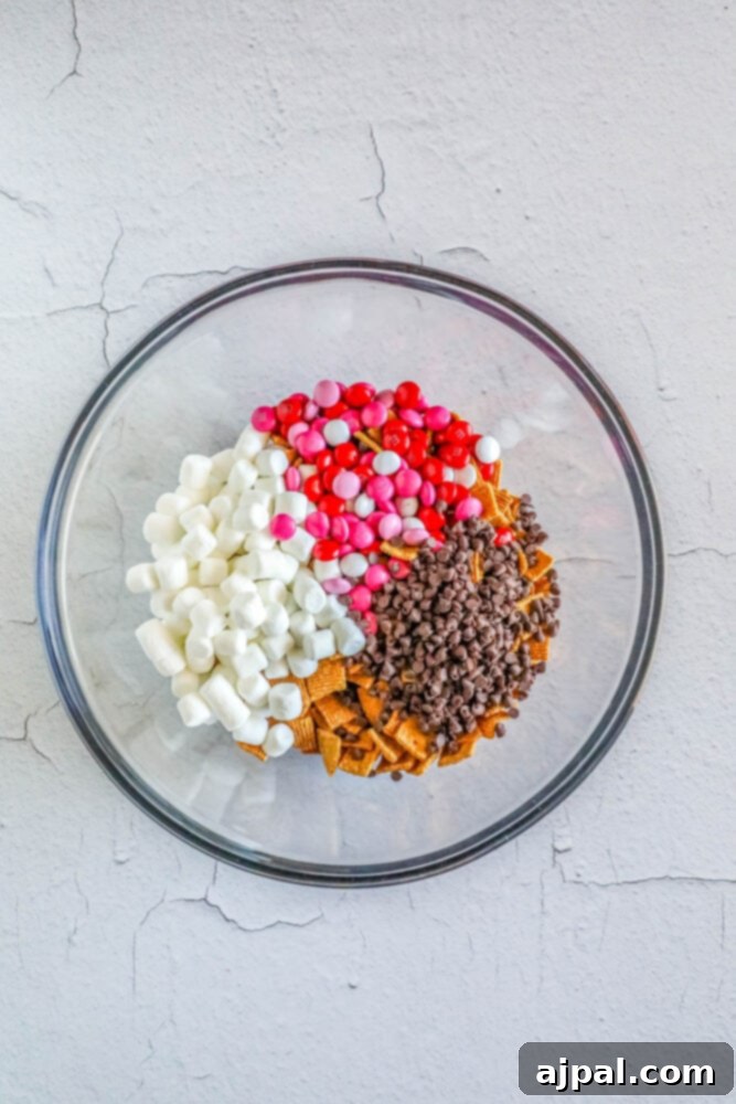 Valentine Smores Snack Mix 6 Golden Grahams cereal, mini marshmallows, pink M&M's, and chocolate chips are gently mixed in a bowl for the Valentine's S'mores Snack Mix.
