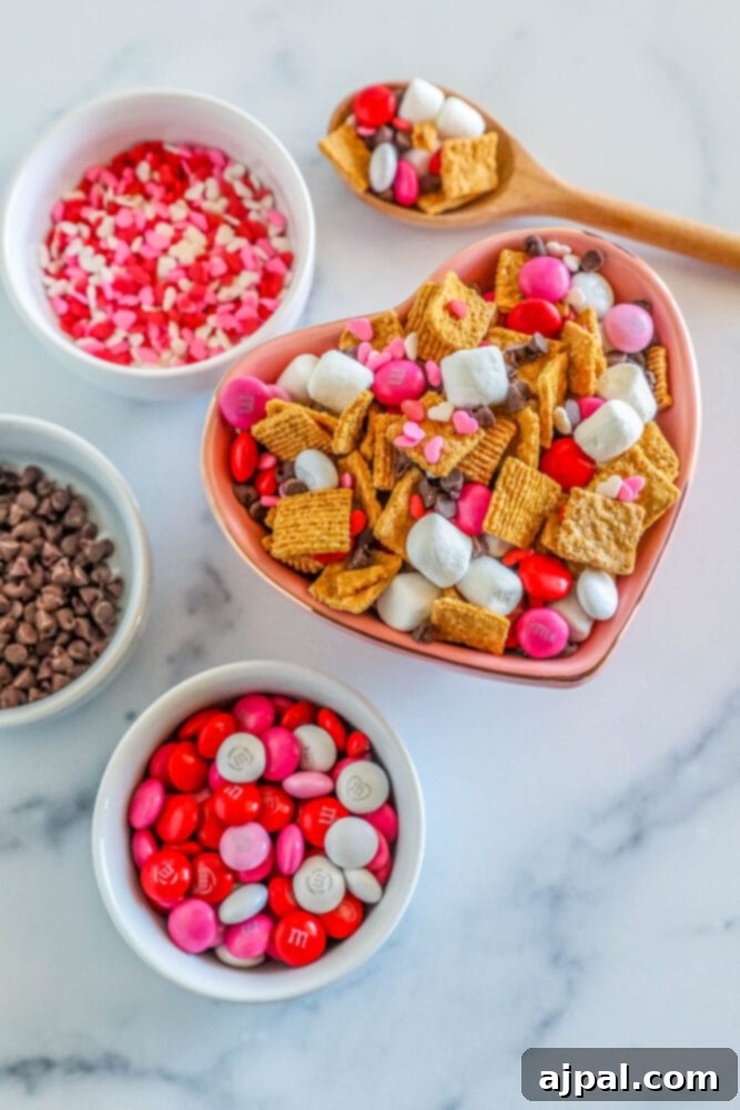 Valentine Smores Snack Mix 8 Close-up of the mixed Valentine's S'mores Snack Mix in a bowl, with smaller bowls of chocolate chips, sprinkles, and M&M's visible in the background, ready for topping or refilling.