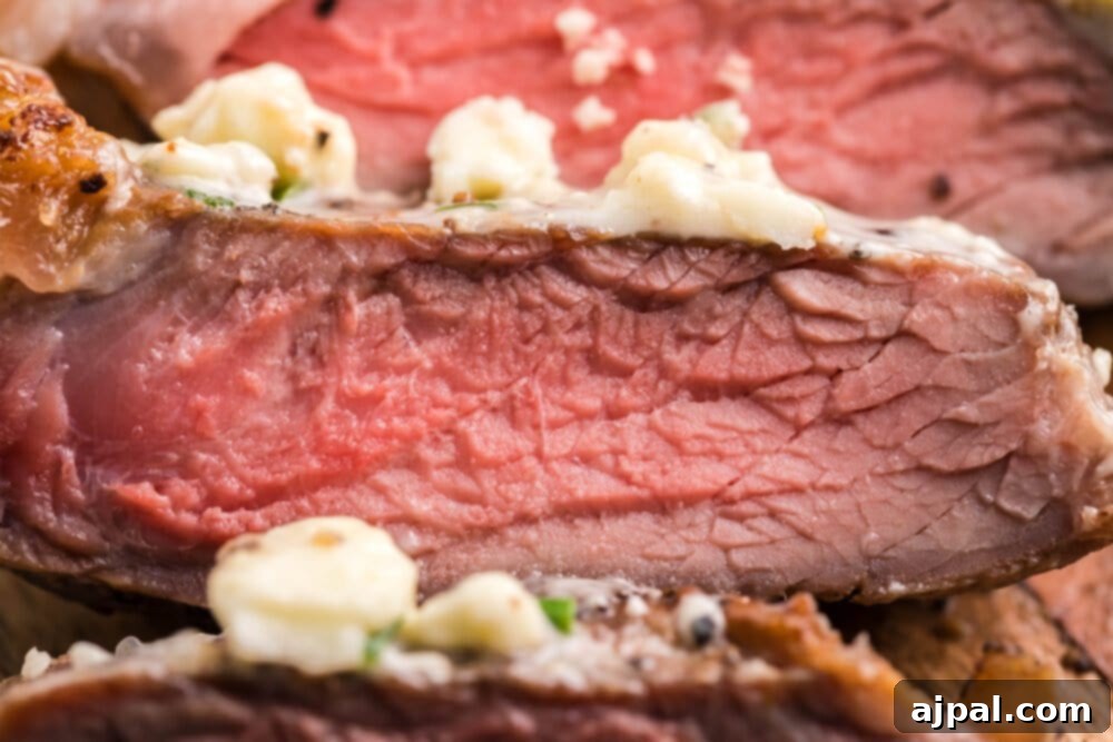 Close-up of a New York Strip steak expertly cooked to medium-rare, topped with melting blue cheese butter and fresh herbs.