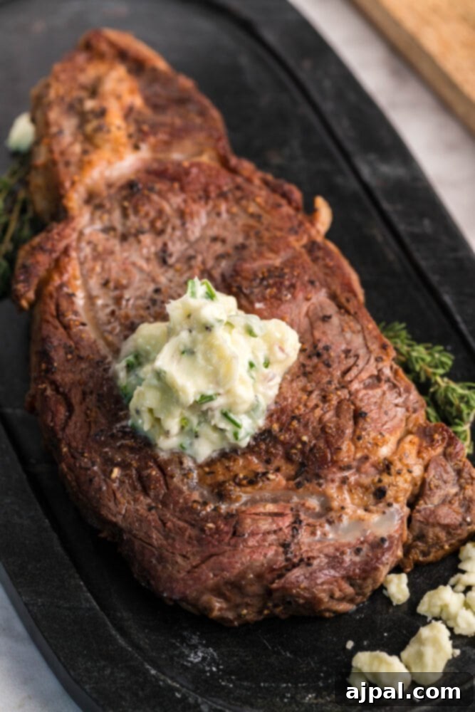 A perfectly seared New York Strip steak on a black plate, generously topped with melted blue cheese butter and garnished with fresh herbs.