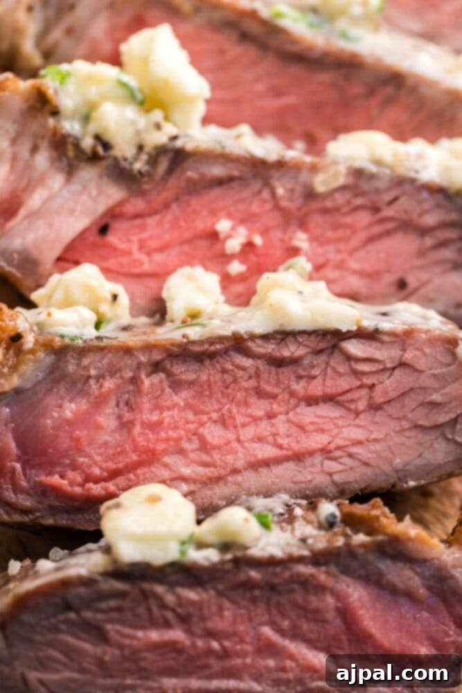 Slices of perfectly cooked New York Strip steak, topped with a dollop of blue cheese butter, on a rustic wooden cutting board.