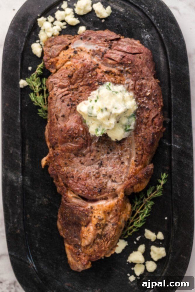 A beautifully cooked New York Strip steak with melting blue cheese butter and fresh thyme on a black plate.