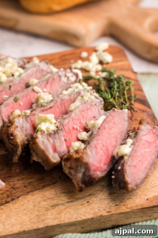 Seared New York Strip steak with a pat of blue cheese butter and fresh thyme sprigs on a wooden board.